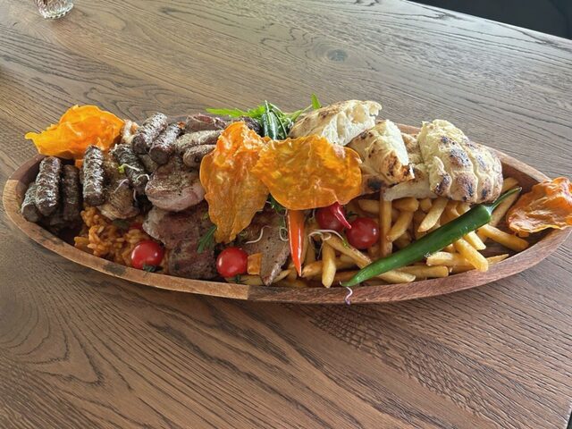 Große gemischte Grillplatte mit Ćevapčići und Spießen auf Holzschale